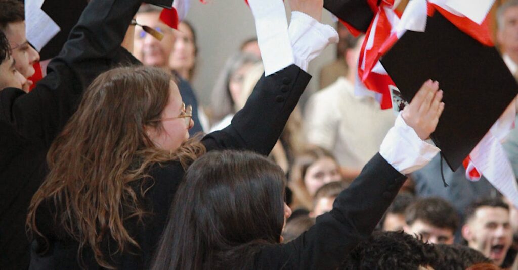 Students celebrate graduation by tossing caps indoors. Joyous academic milestone.